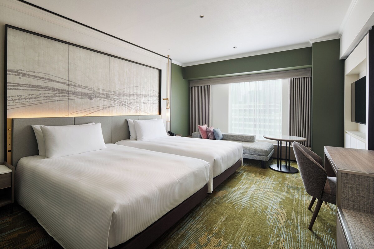 A hotel room with two beds, a seating area, a dining table, and a large window with curtains.