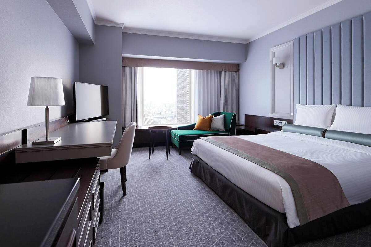 Une chambre d’hôtel avec un lit, un bureau, une chaise et une vue sur la ville par la fenêtre.