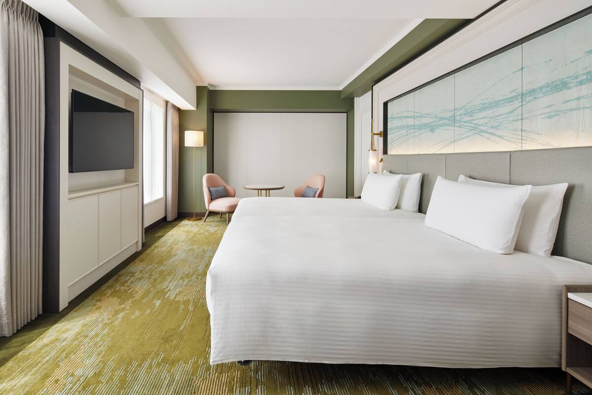 Une chambre d’hôtel avec un grand lit, deux fauteuils, une télévision et un tableau au mur.