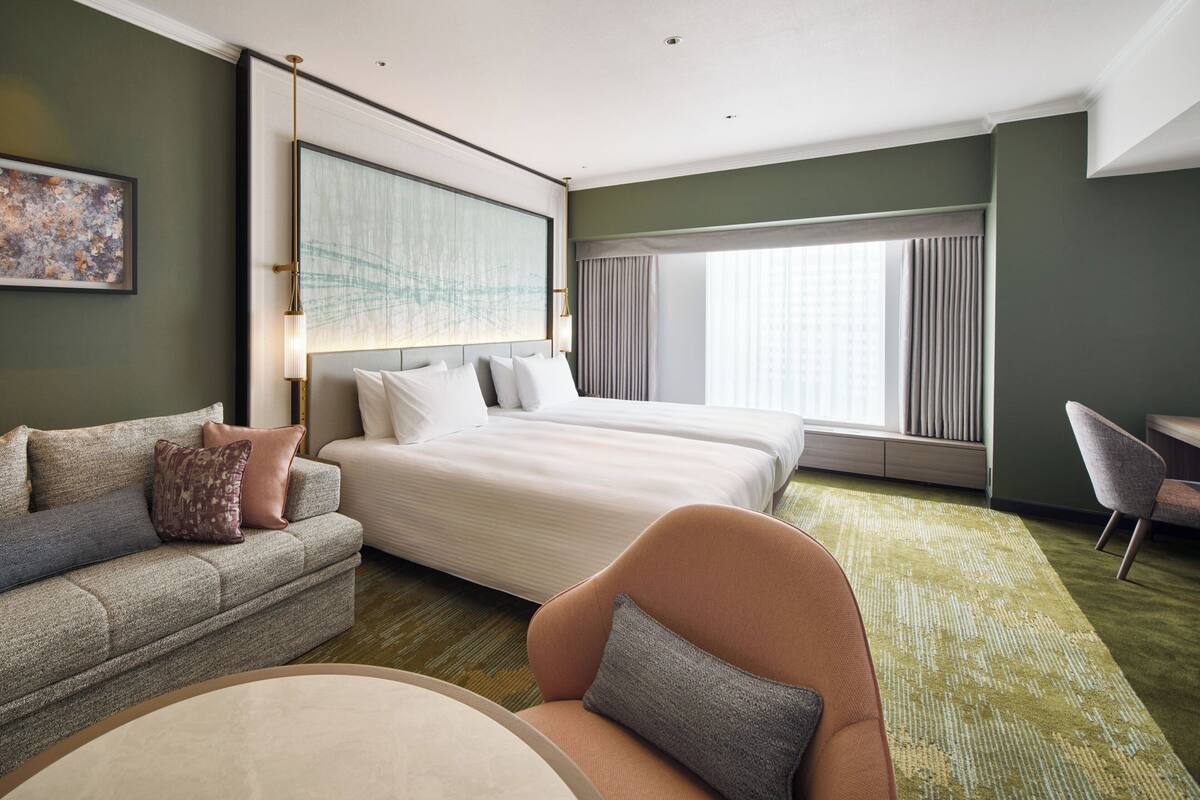 Une chambre d’hôtel avec un grand lit, un canapé, un fauteuil et une vue sur la ville par la fenêtre.
