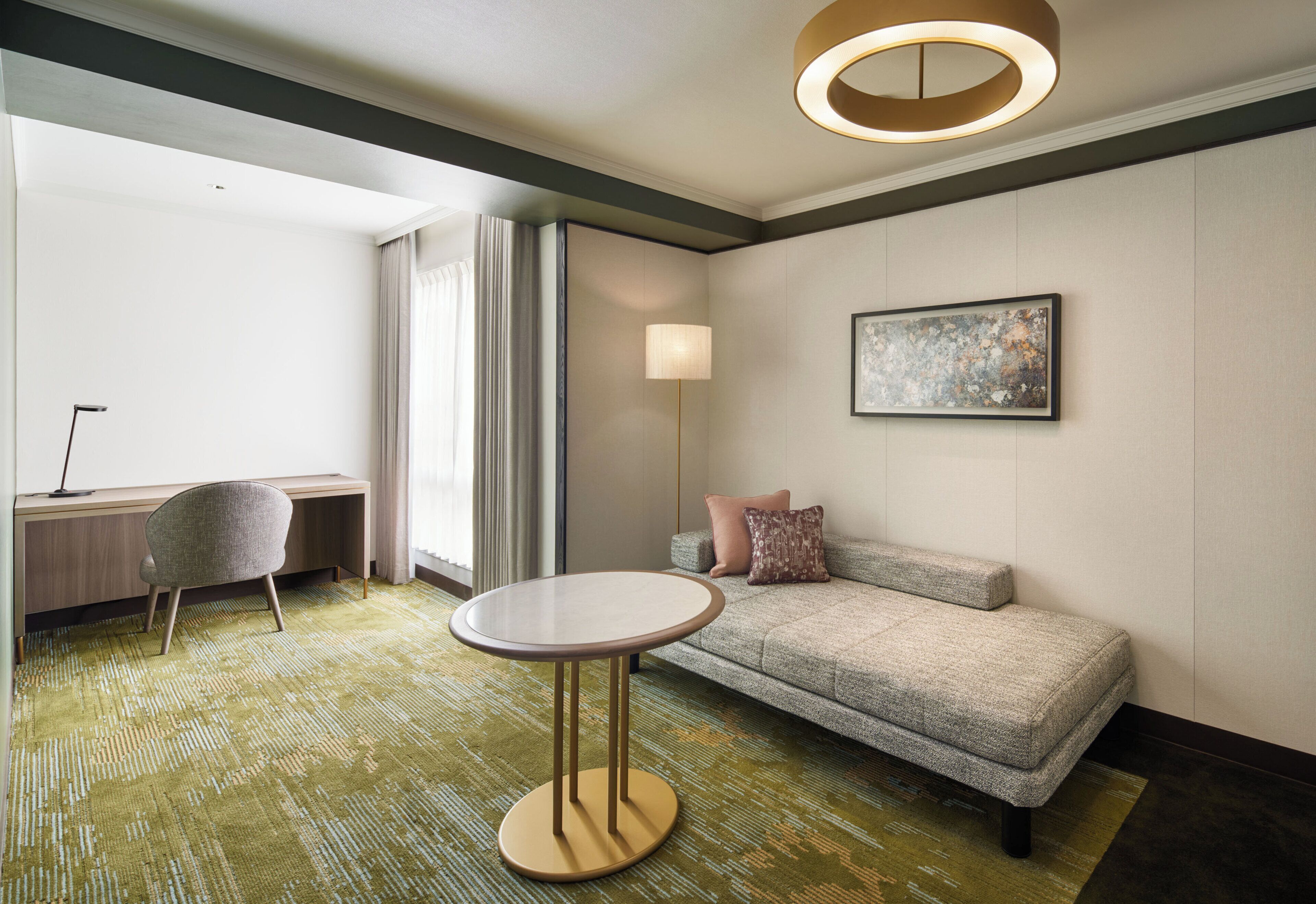 A modern hotel room with a sofa, a round table, a desk, and a lamp.