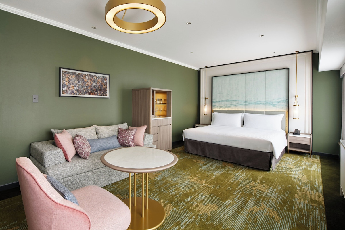 A modern hotel room with a large bed, a sofa, a small table, and a cabinet.