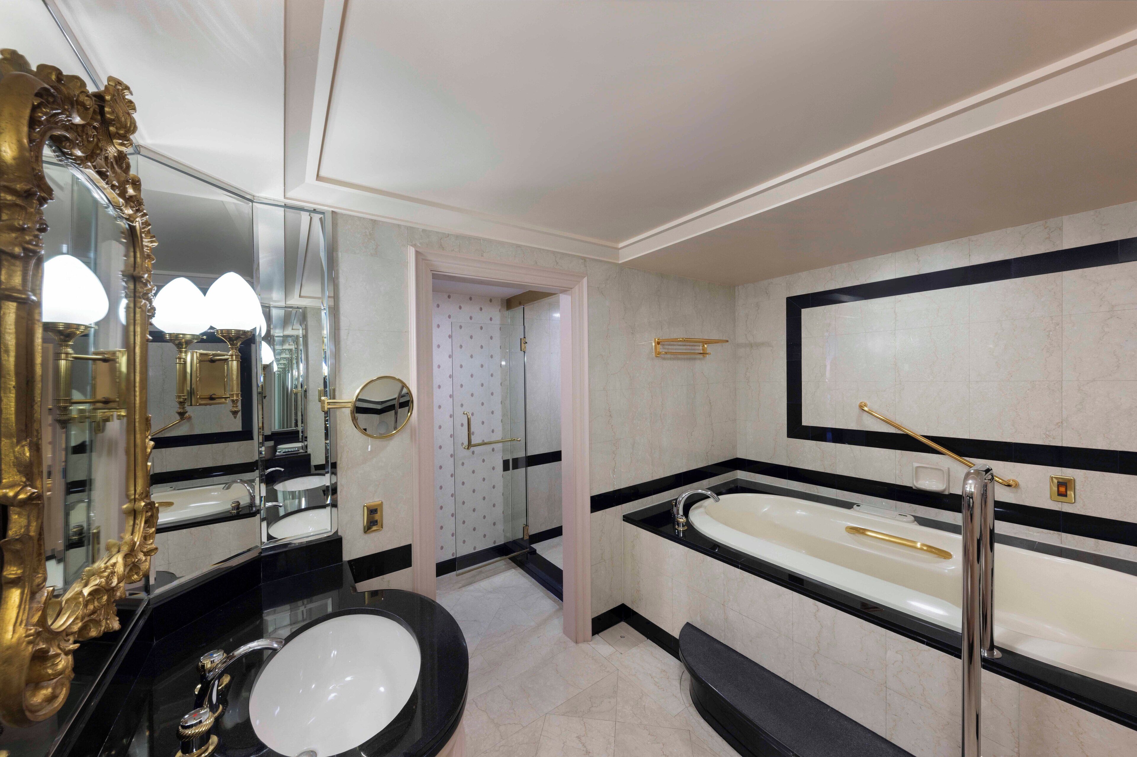 A luxurious bathroom with a large mirror, two sinks, a bathtub, and a shower.