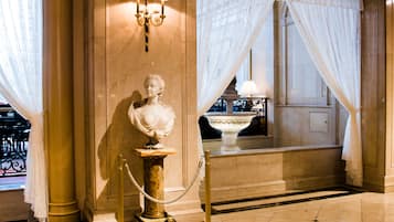 Una estatua de mármol sobre un pedestal, una fuente y una habitación con suelo de mármol y cortinas.