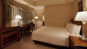 A hotel room with a large bed, a wooden dresser, a desk, and two lamps.