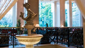 A grand lobby with a marble fountain, ornate iron railings, and large windows offering views of trees. - RIHGA Royal Hotel Tokyo (Tokyo)