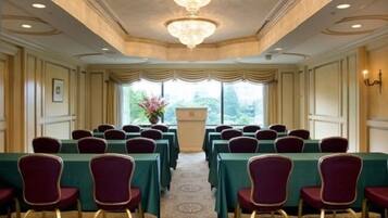 A conference room with rows of tables and chairs, a chandelier, and a view of greenery outside.
