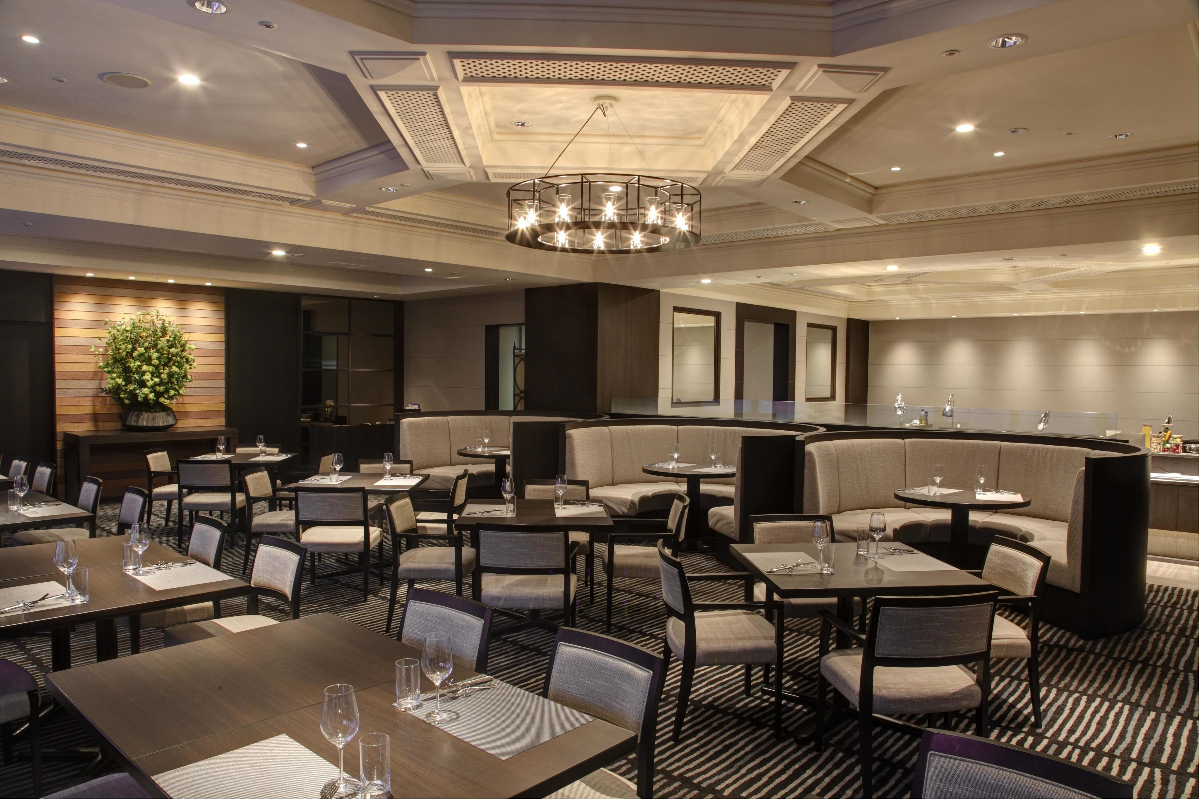 A hotel dining area with multiple seating arrangements, including tables and booths, and a central chandelier.