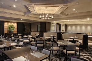 A hotel dining area with multiple seating arrangements, including tables and booths, and a central chandelier.