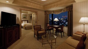 A hotel room with a television, a sofa, a dining table with chairs, a chandelier, and a view of a cityscape at night. - RIHGA Royal Hotel Tokyo (Tokyo)