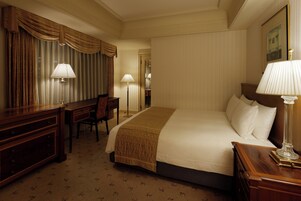 A hotel room with a bed, a desk, a chair, and two lamps.
