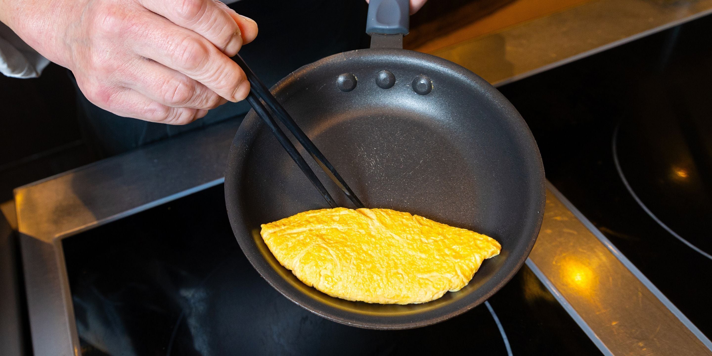 A person holding a frying pan with a folded omelette inside.