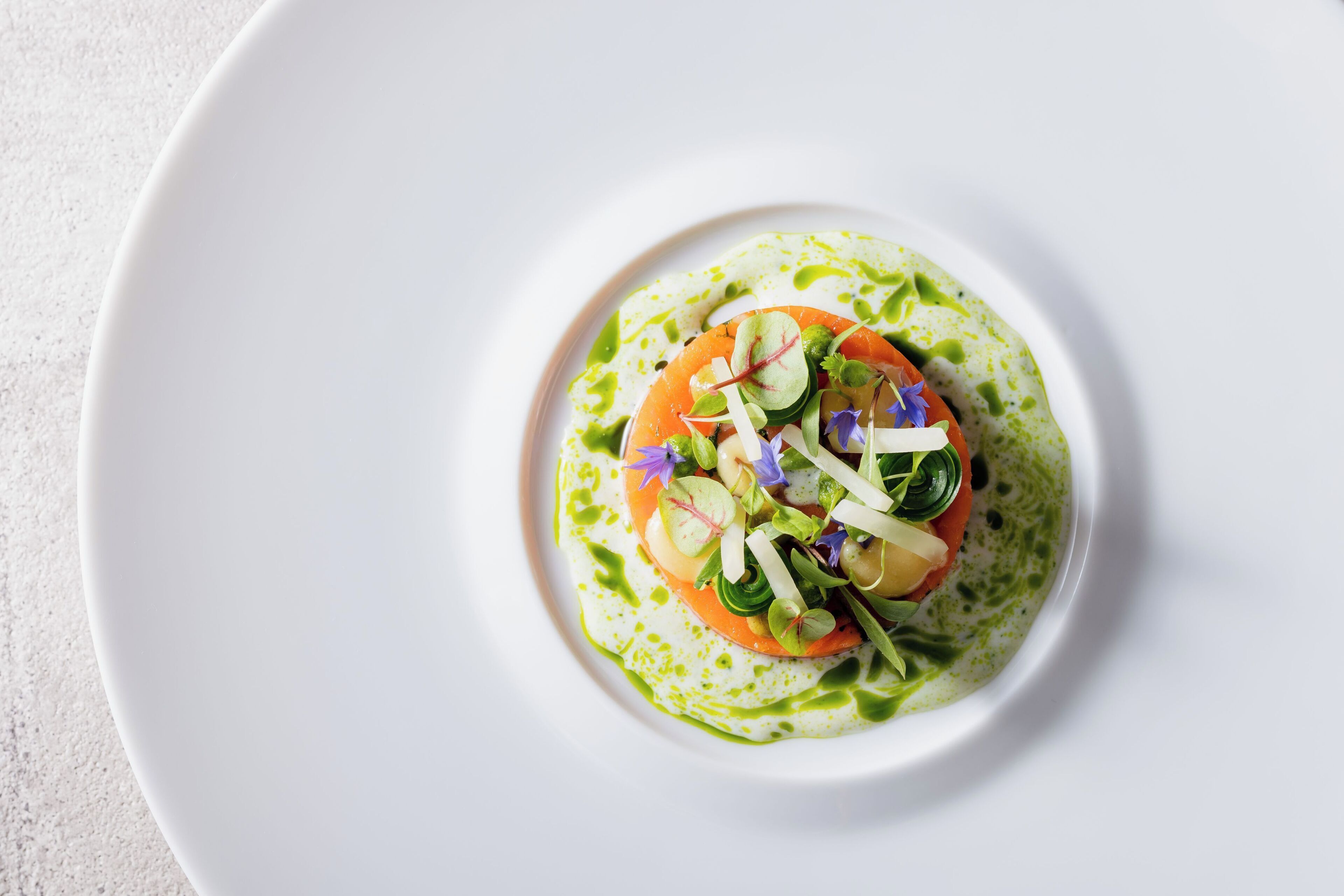 Une assiette blanche avec une sauce verte et une salade composée de tomates et de légumes verts.