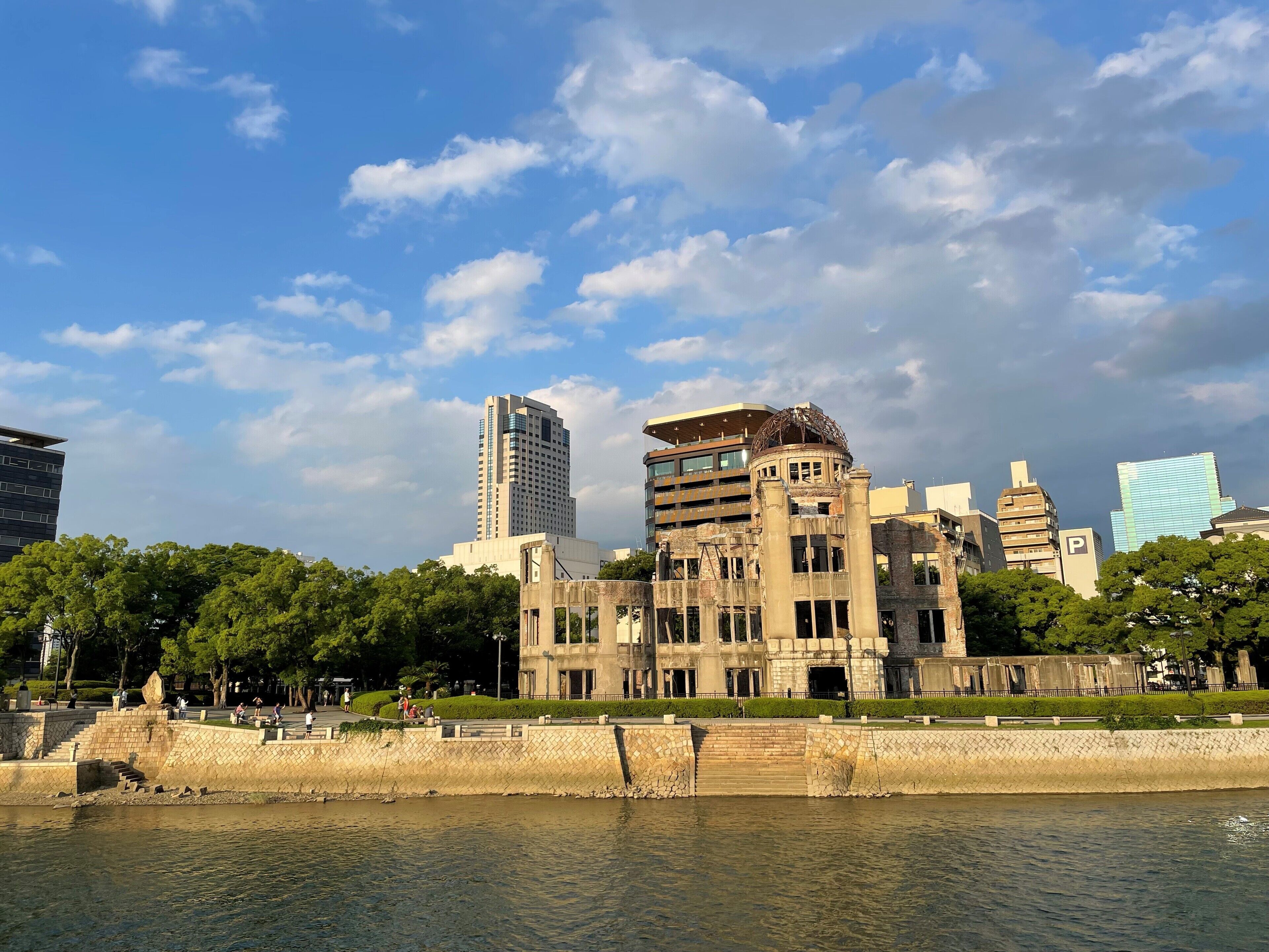 Uitzicht op een rivier met een historisch gebouw, moderne wolkenkrabbers en een park vol mensen.