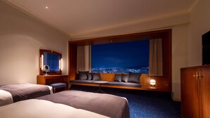 A hotel room with two beds, a seating area with a city view, a television, and a desk with a mirror. - RIHGA Royal Hotel Hiroshima (Hiroshima)