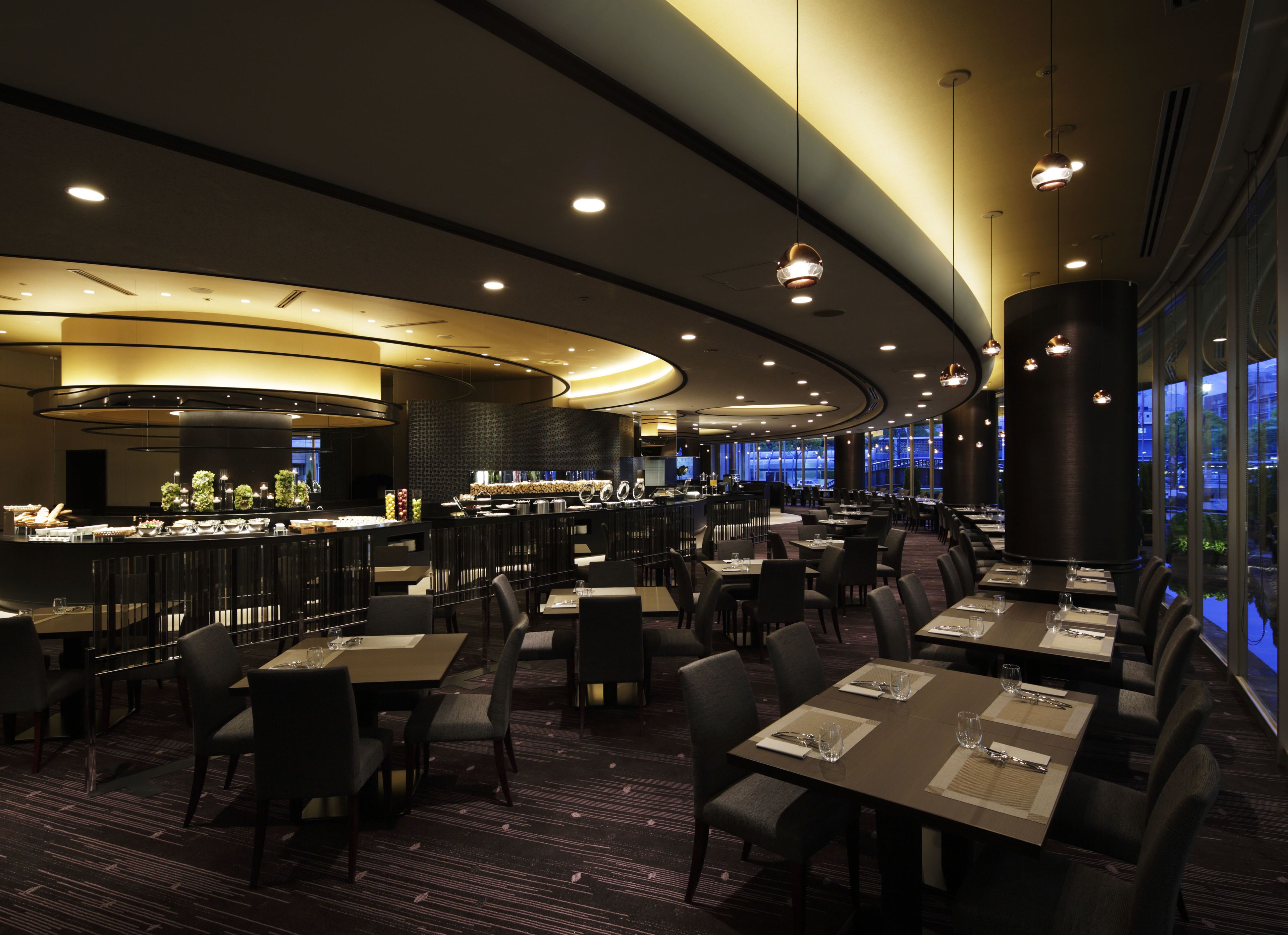 Un restaurante moderno con una barra curva, varias mesas de comedor y vistas de la ciudad a través de amplios ventanales.