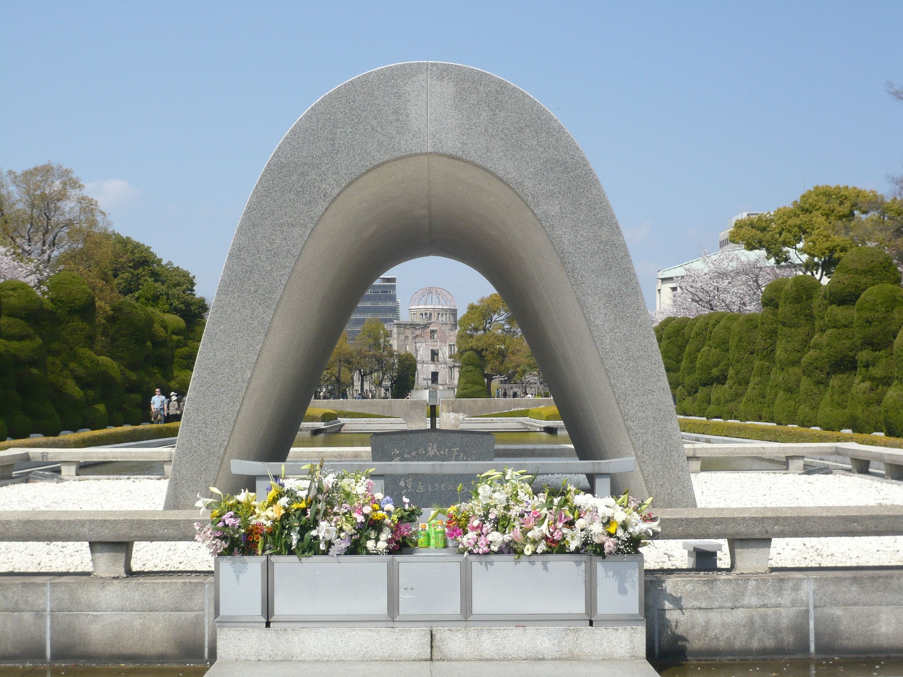 A memorial with a large arch structure, surrounded by well-maintained greenery and a clear sky.