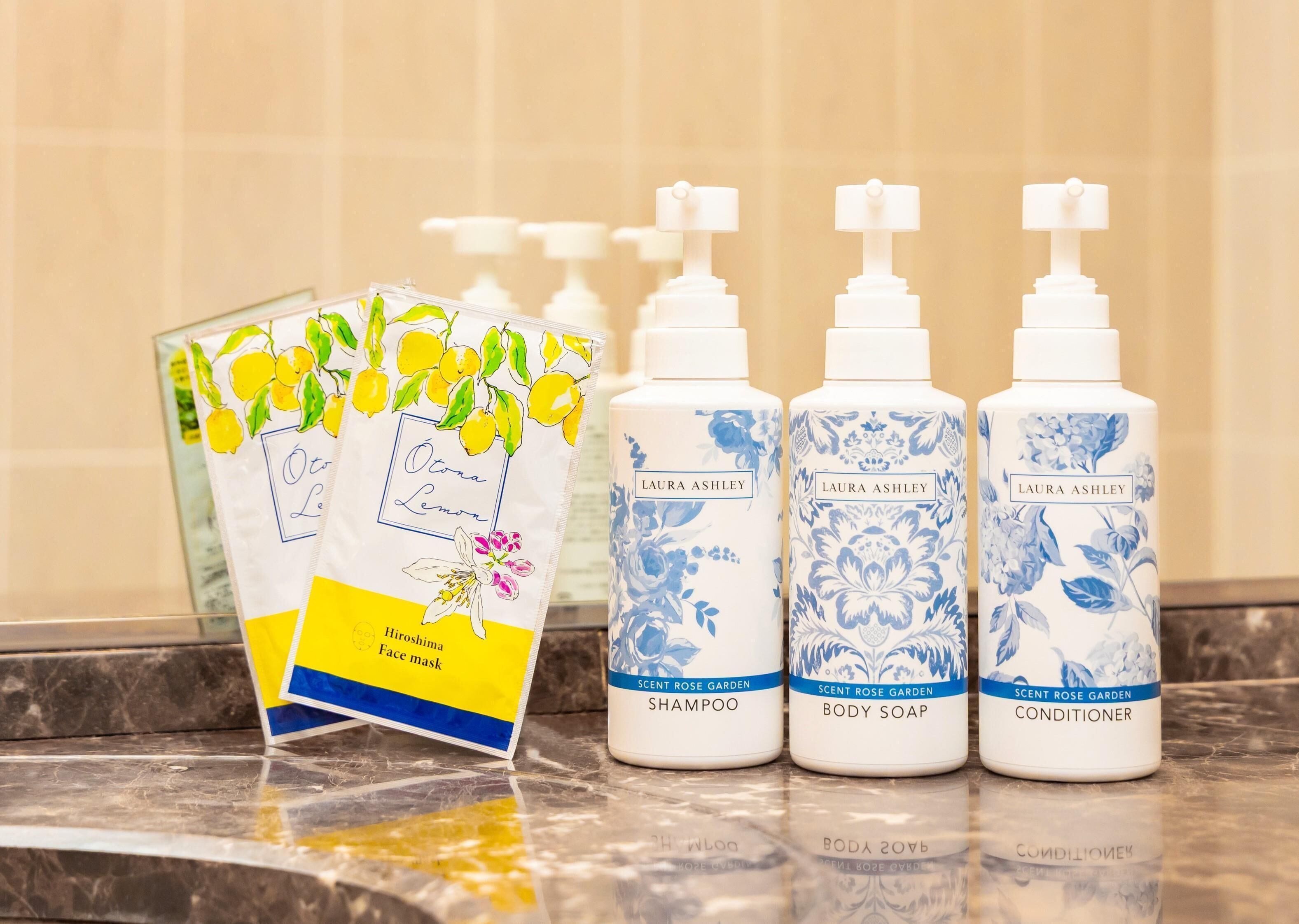 Un taulell de bany amb tres ampolles de productes per a la cura corporal de Laura Ashley i un paquet de mascareta per a la cursa de Hirosima.