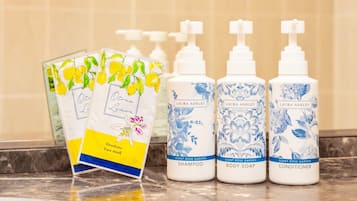 Un taulell de bany amb tres ampolles de productes per a la cura corporal de Laura Ashley i un paquet de mascareta per a la cursa de Hirosima.
