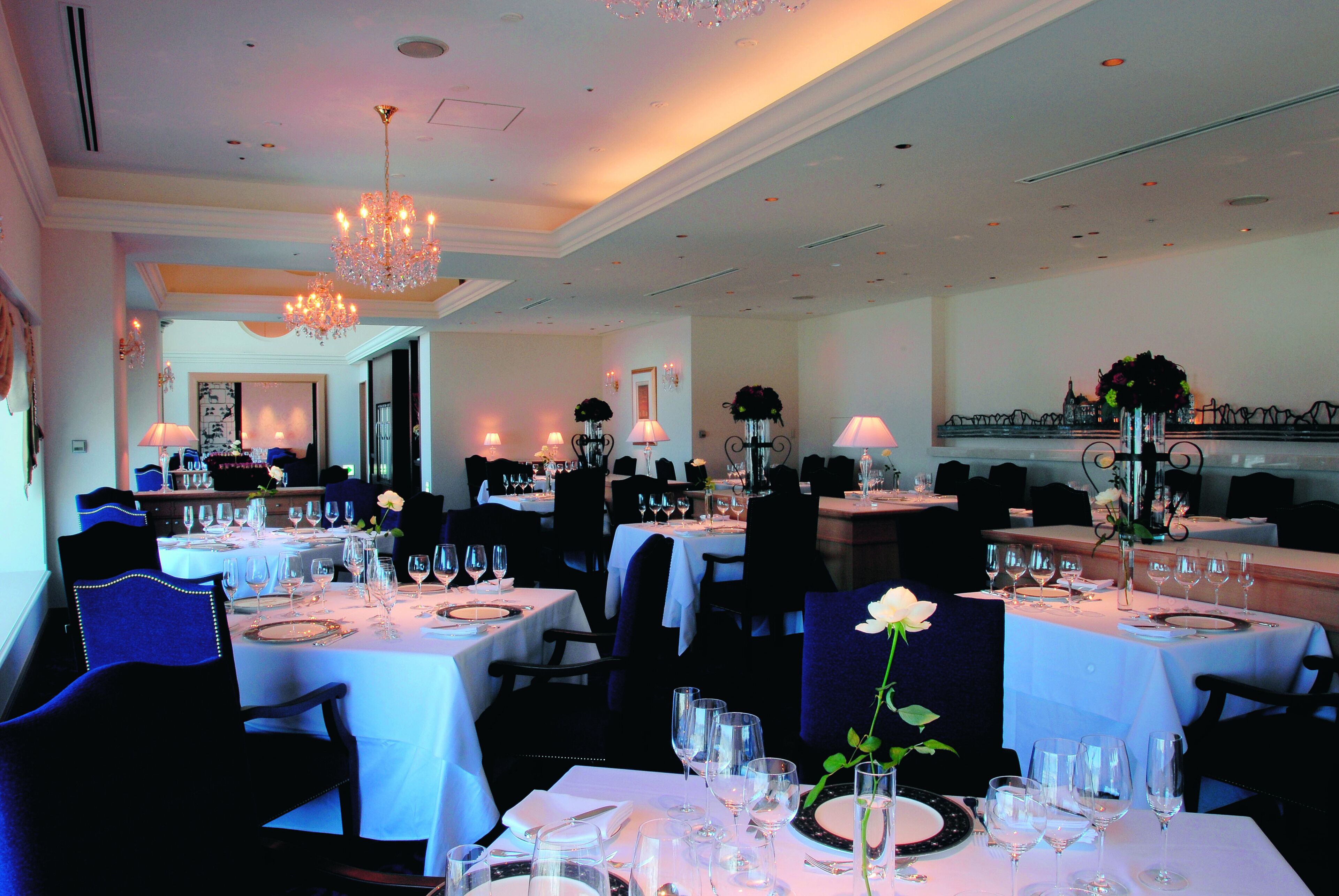 A dining area with multiple tables set for service, each with a white tablecloth, silverware, and wine glasses.