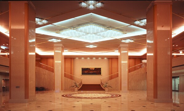 Un hall espacioso con una imponente escalera, un candelabro y un cuadro grande en la pared.