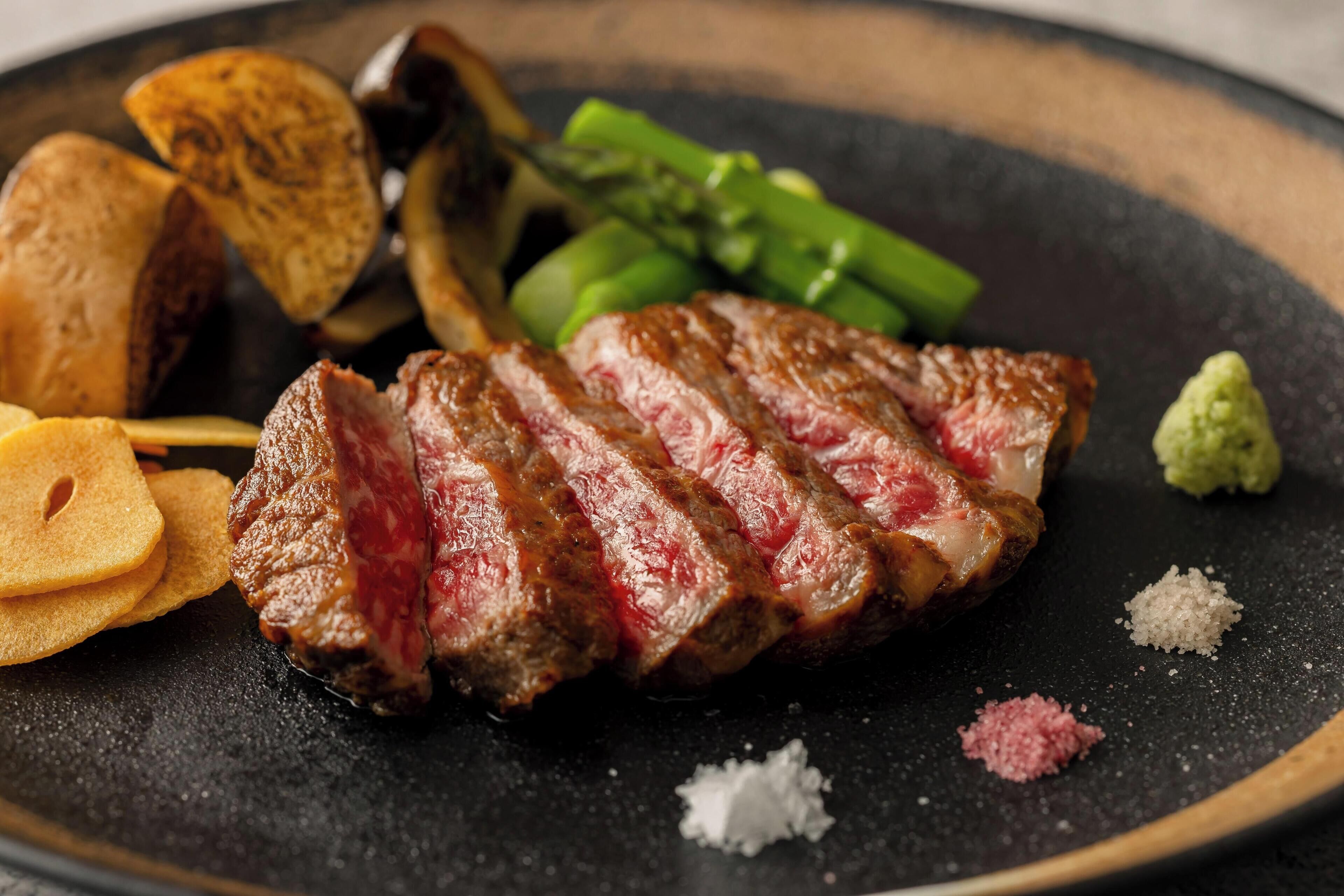 Un plato con bistec en rodajas, espárragos y papas asadas.
