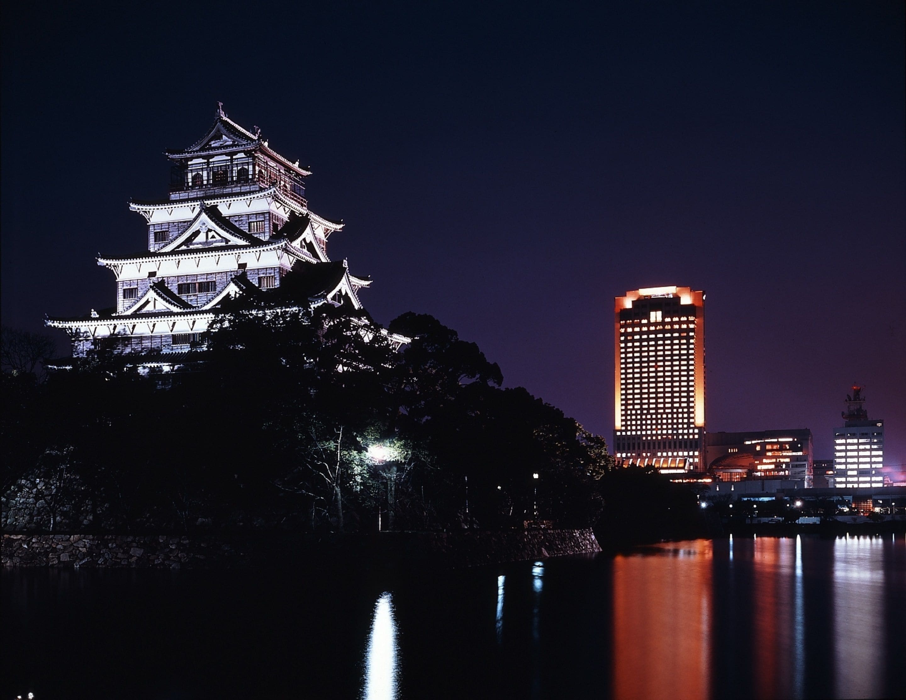 A traditional Japanese castle with multiple tiers and a modern high-rise building in the background.