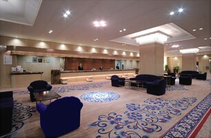 Un hall de hotel con mostrador de recepción, zona de estar y alfombra decorativa.