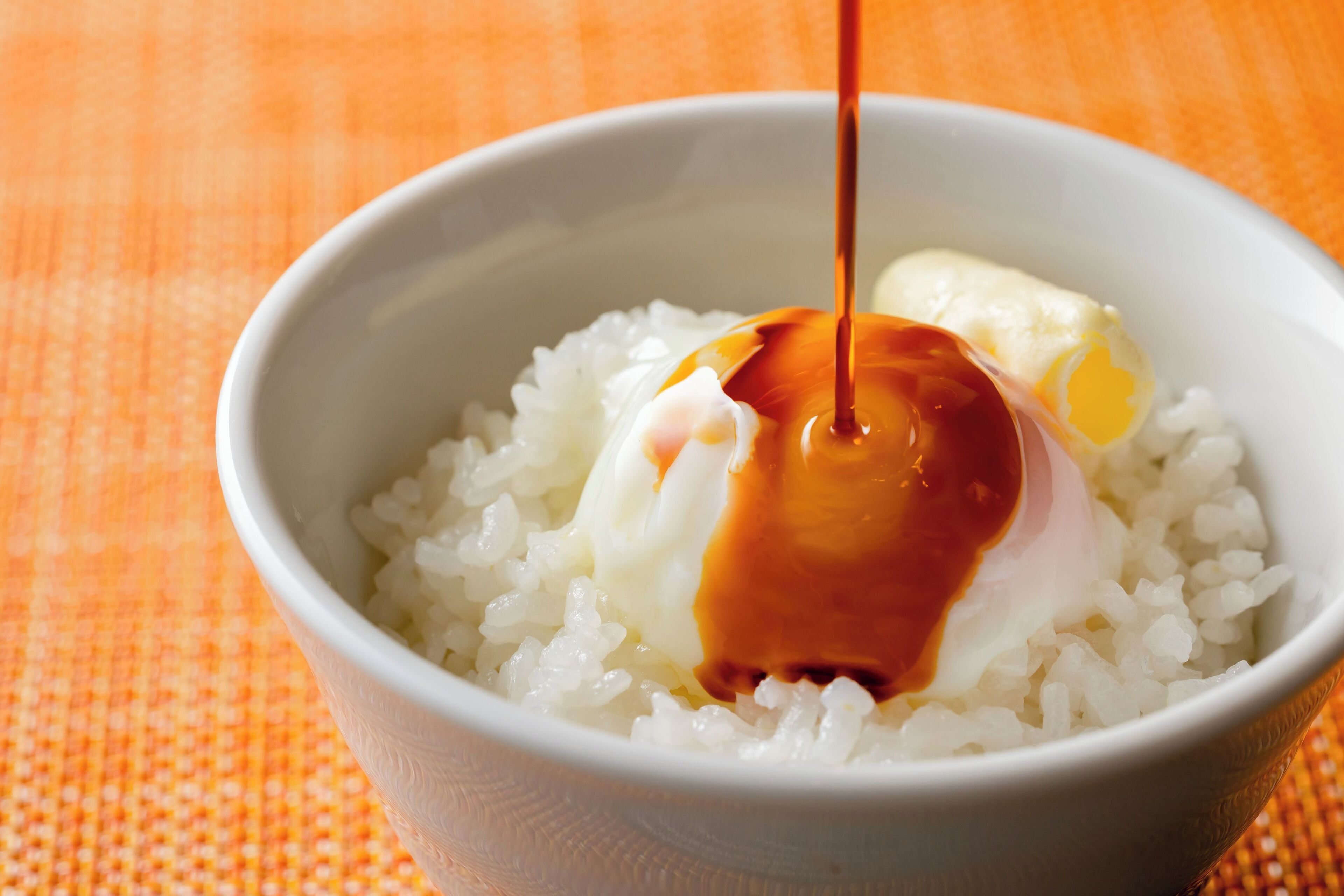 A bowl of white rice with a poached egg and a drizzle of sauce.