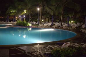 A nighttime pool area with lounge chairs and palm trees. - La Palm Royal Beach Hotel (Accra)