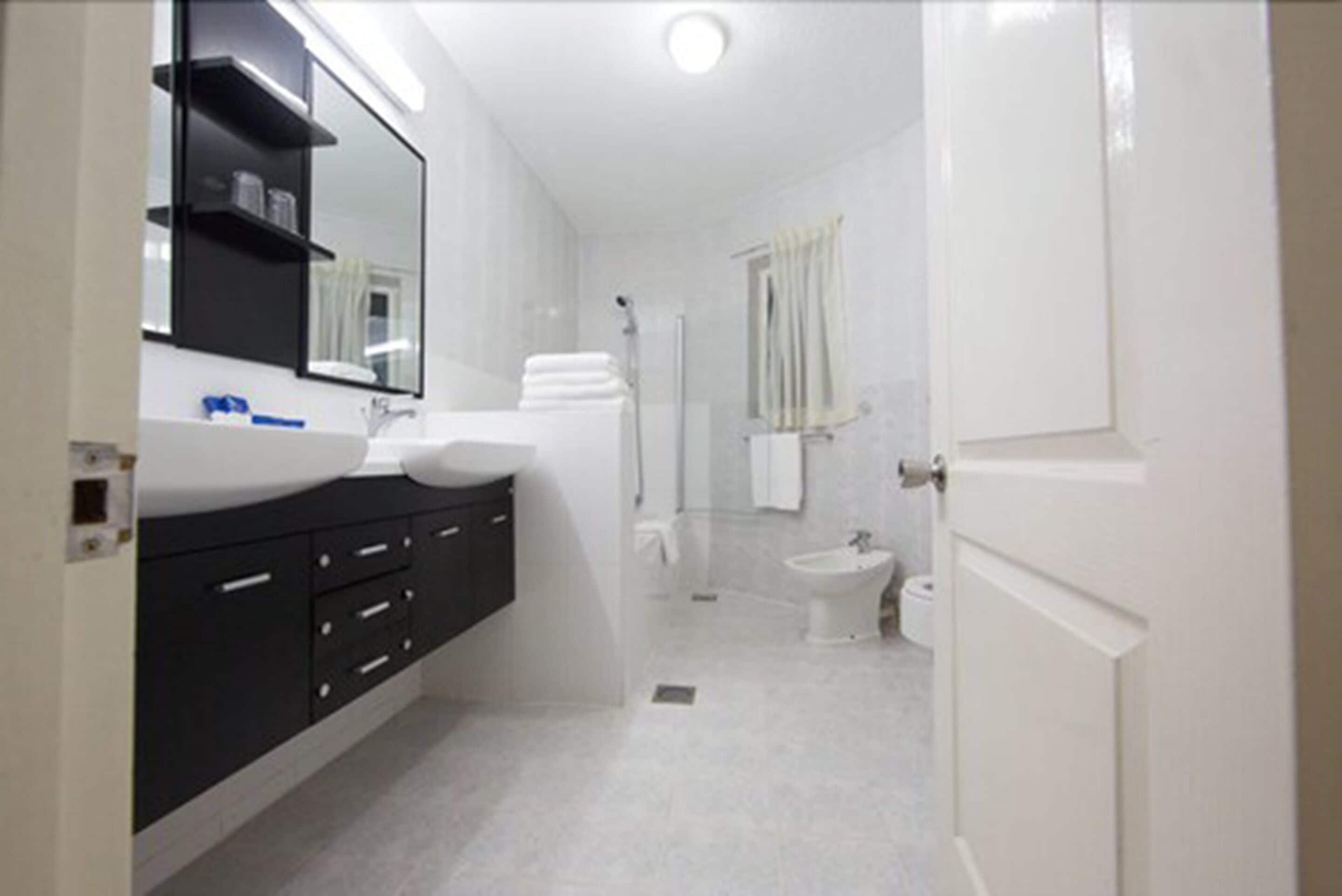 Un baño moderno con un espejo grande, lavamanos blanco y armarios negros.