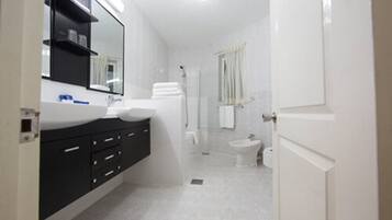 Un baño moderno con un espejo grande, lavamanos blanco y armarios negros.