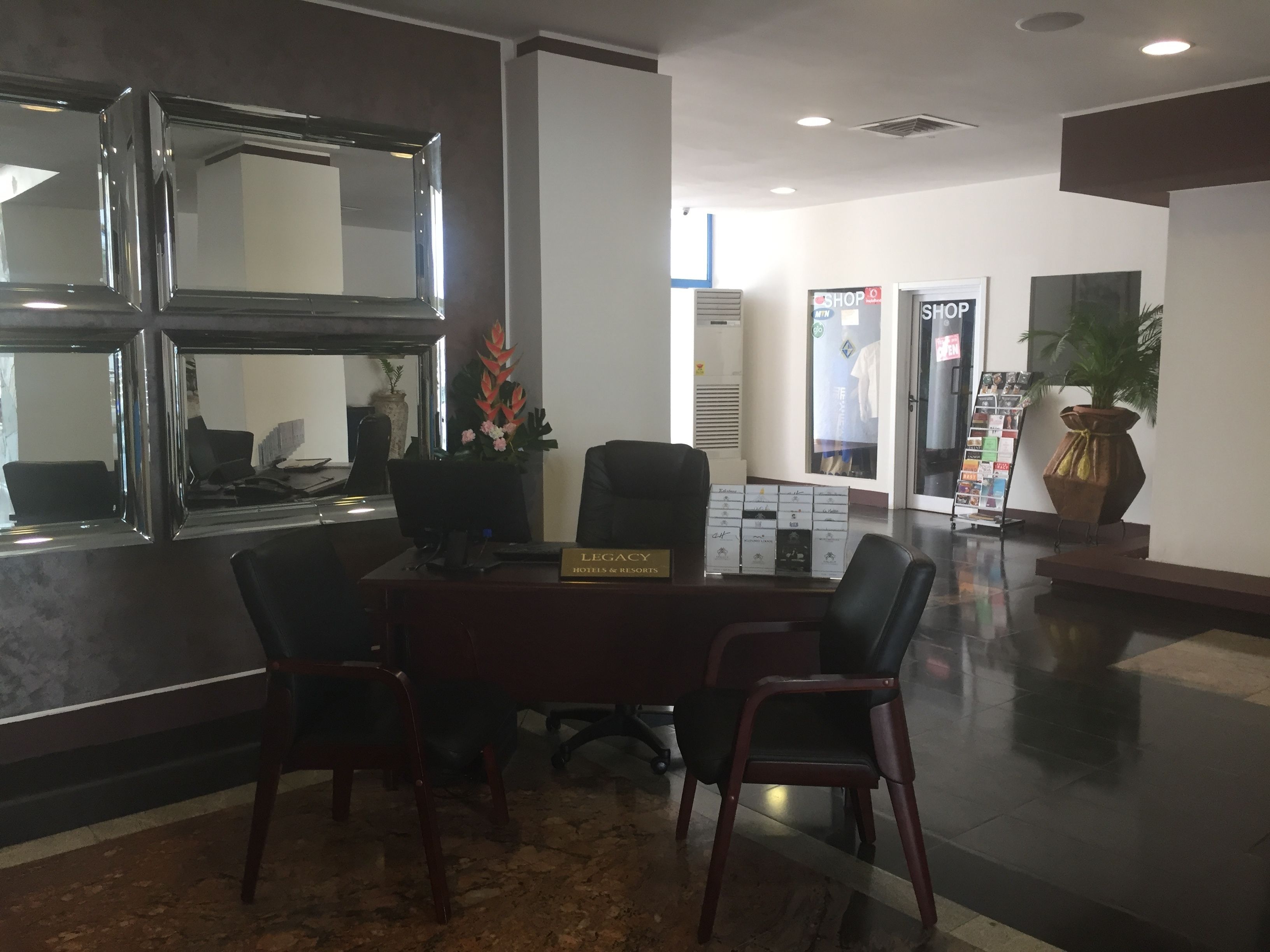 Zona de recepción con escritorio, sillas, espejo, planta en maceta y cartel con el nombre del hotel.