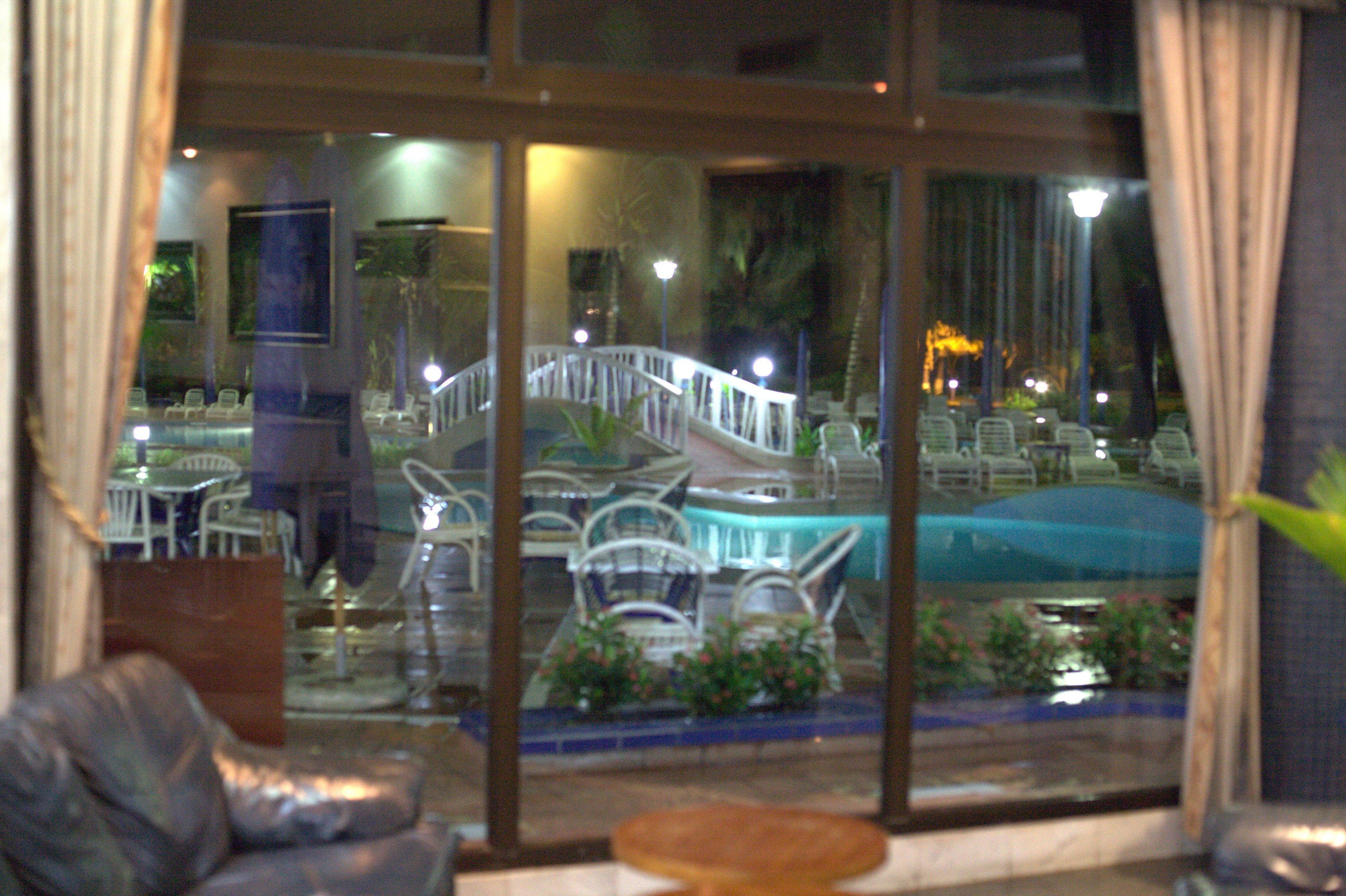A view through a window of a hotel lobby with a pool, chairs, and a staircase.