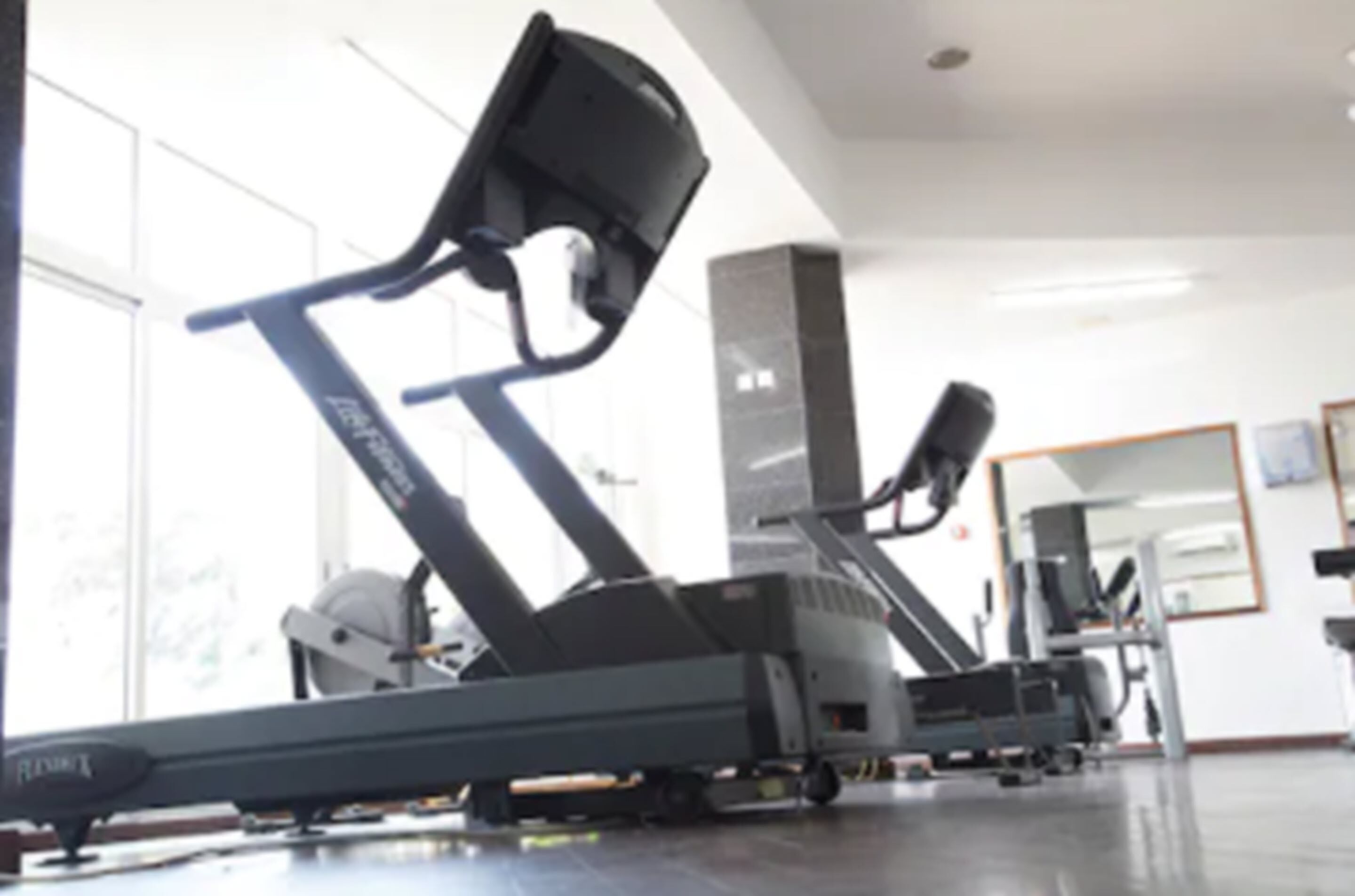 A gym with exercise equipment, large windows, and a mirror on the wall.