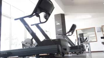 A gym with exercise equipment, large windows, and a mirror on the wall.