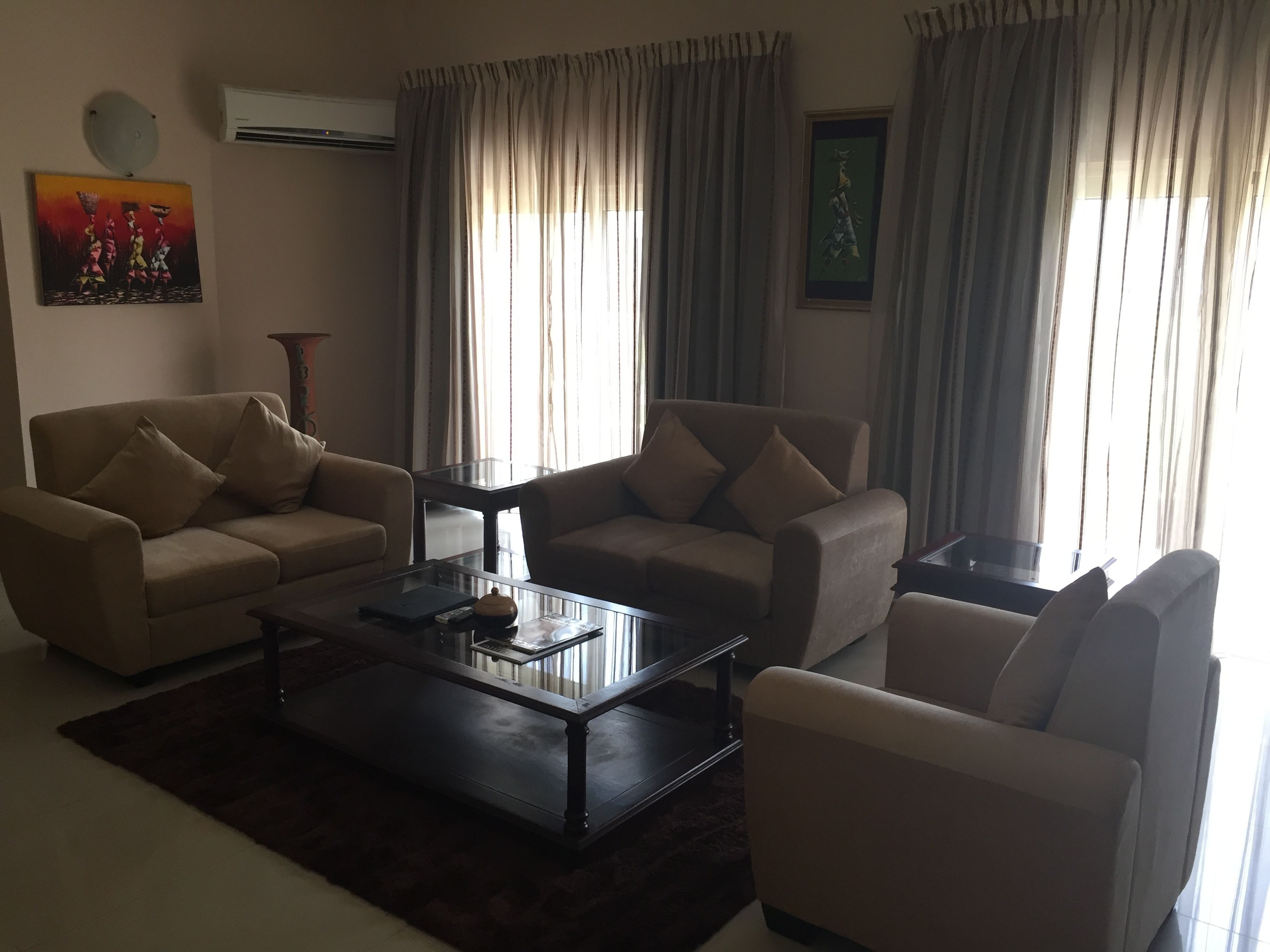 A living room with two sofas, a coffee table, and a TV. There are curtains, a painting, and an air conditioning unit.