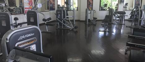 Un gimnasio con diversos equipos de ejercicio, incluyendo cintas de correr, máquinas de pesas y una máquina de remo.