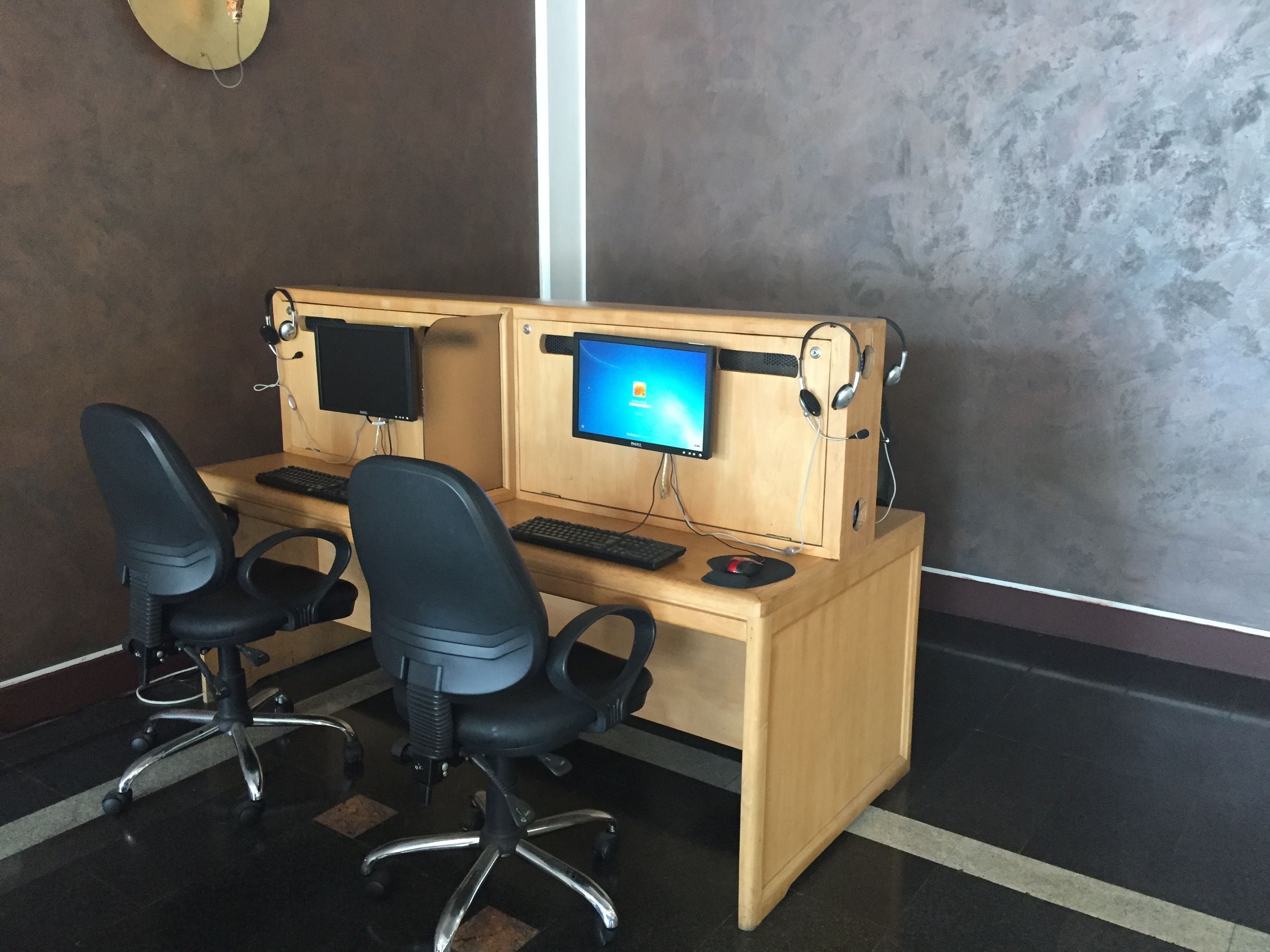 A wooden desk with two monitors, a keyboard, and two black office chairs.