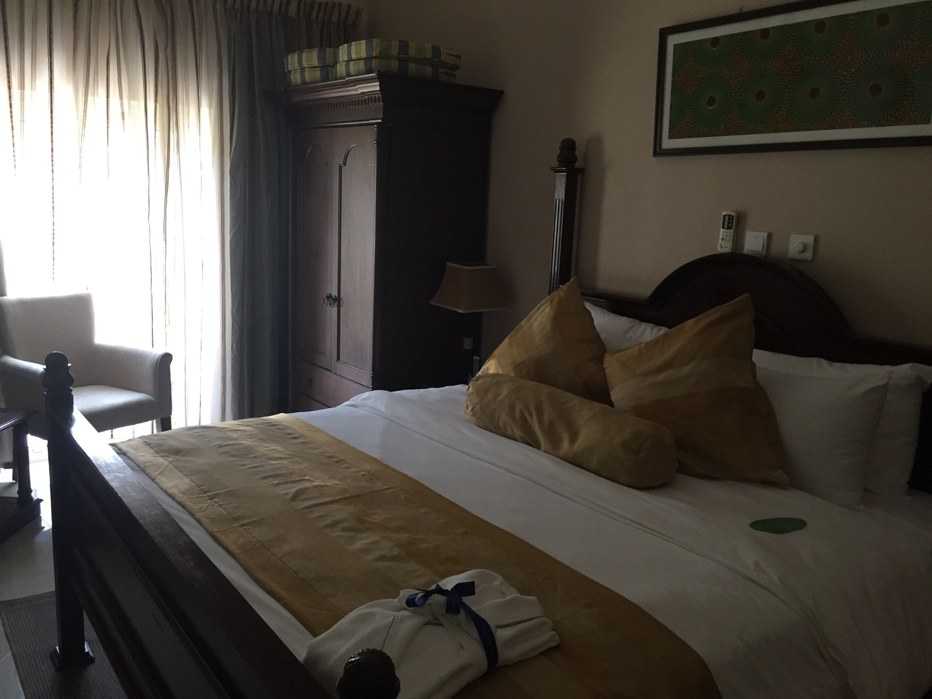 A hotel room with a bed, a chair, a wardrobe, and a lamp.