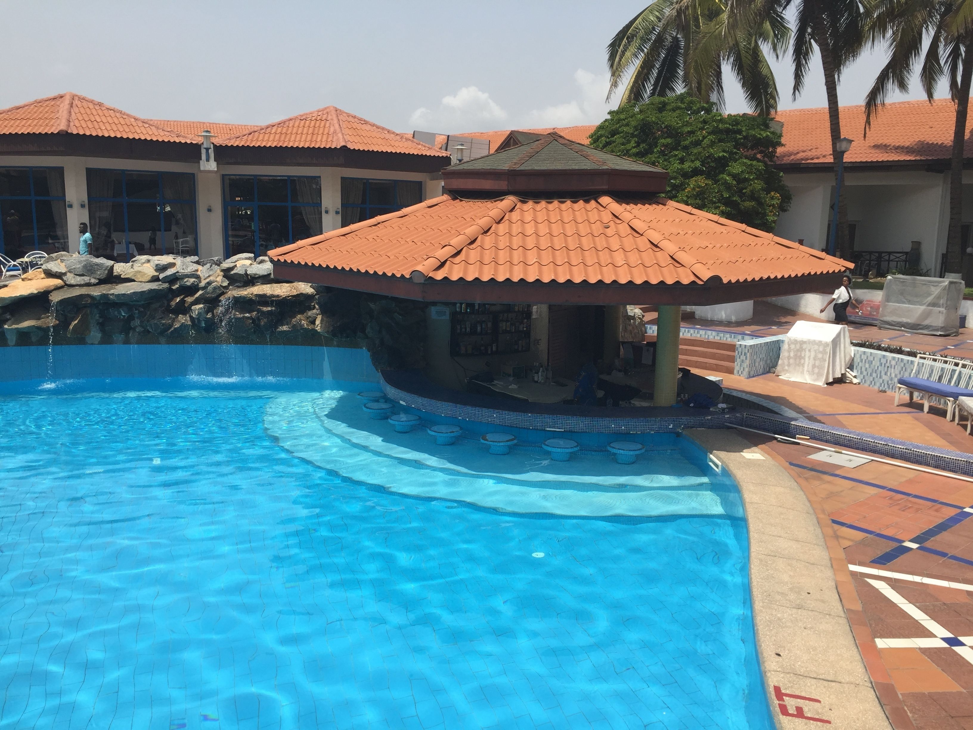 A swimming pool with a tiled deck, a small bar area, and a covered seating area.