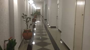 A hotel corridor with a checkered floor, potted plants, and doors on both sides.