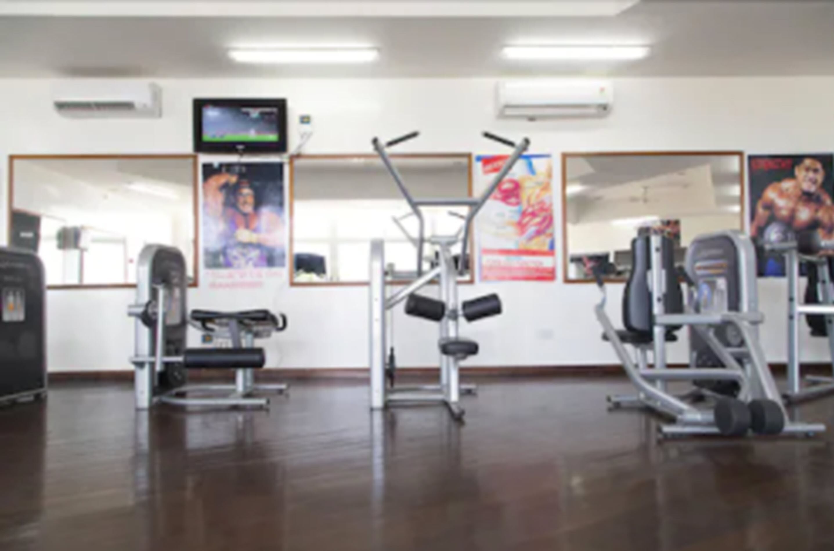 A gym with various exercise equipment, a television on the wall, and posters on the walls.