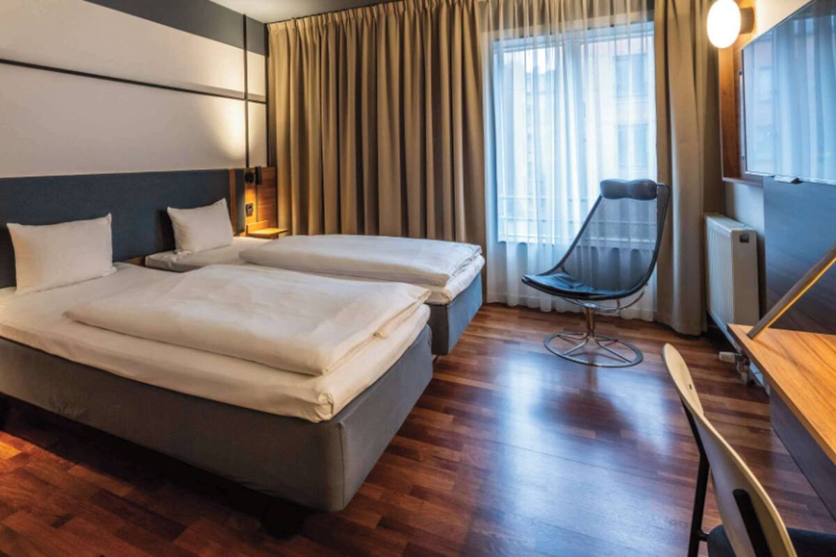 Una habitación de hotel con una cama grande, un escritorio, una silla y una ventana con cortinas.