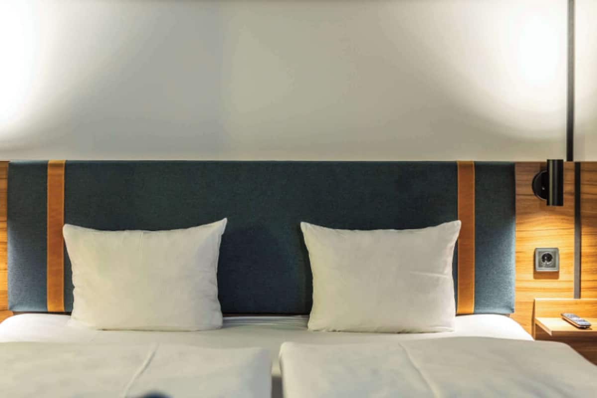 Una cama doble con dos almohadas, un cabecero de madera y dos mesitas de noche con lámparas.