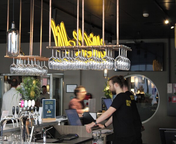 Un espace bar avec de nombreux verres à vin suspendus au plafond, un comptoir de bar doté de robinets et un ordinateur portable posé sur le comptoir.