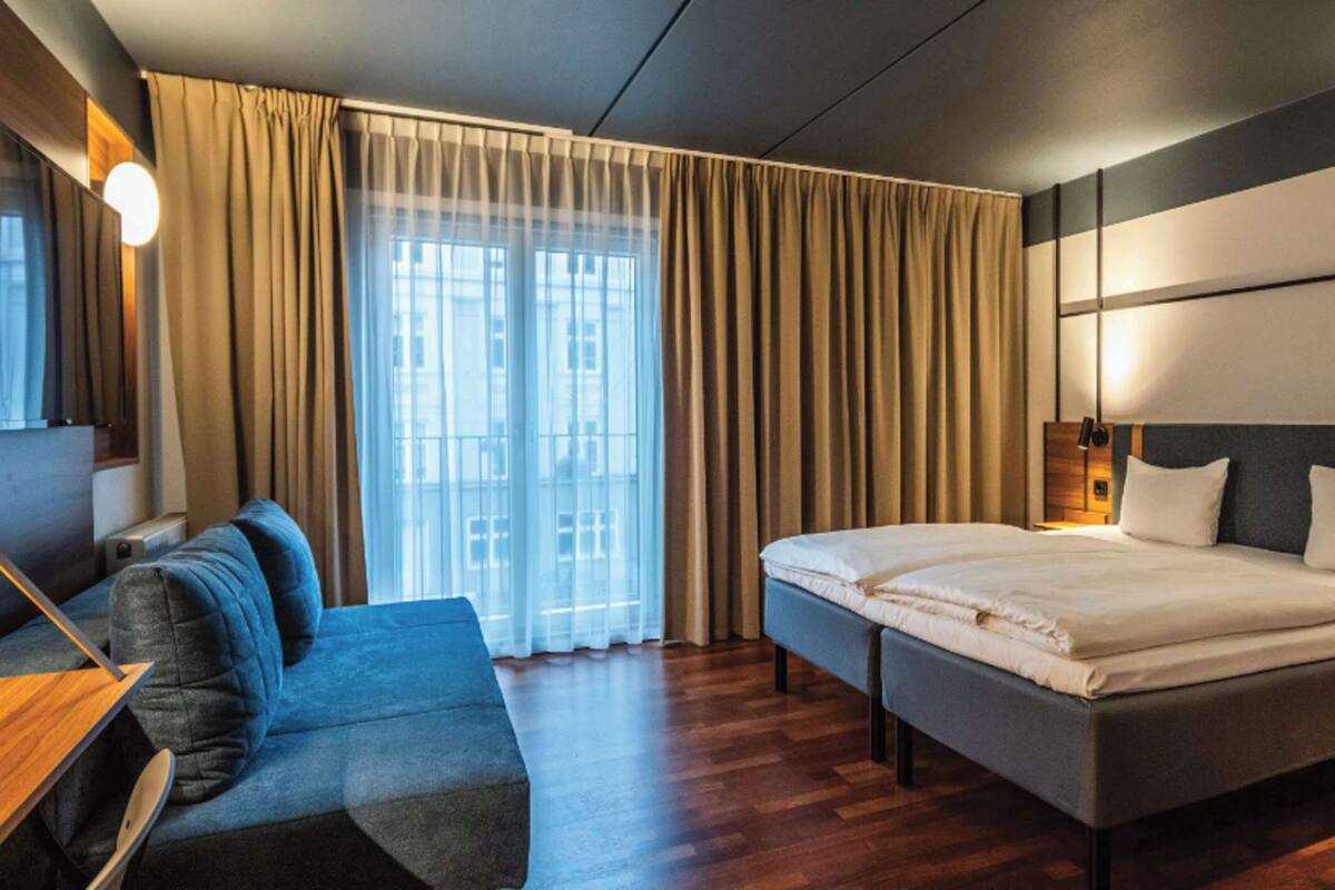 Una habitación de hotel moderna con una cama, un sofá y un ventanal con cortinas.