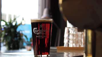 Et glas Carlsberg på en bardisk med en sløret byudsigt og en plante i baggrunden.