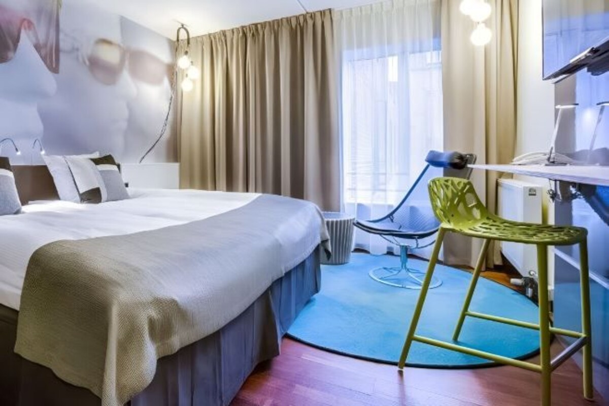 Une chambre d’hôtel avec un lit, un bureau, une chaise et une grande fenêtre avec des rideaux.
