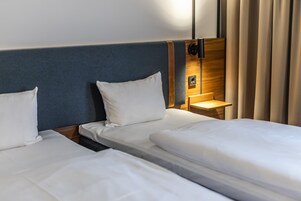 Habitación de hotel con dos camas individuales, cabecera de madera, mesita de noche y lámpara.